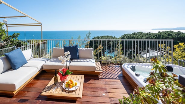 A wooden deck with a sofa, a hot tub, and a table with fruit and a bottle.