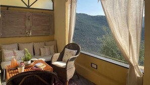 A balcony with a view of a mountainous landscape, a wicker chair, a small table with books and a plant, and a wooden cabinet. - Casa Norvegia by Interhome (Valloria)