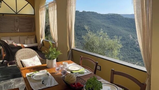A dining area with a table set for two, a sofa, and a view of a mountainous landscape. - Casa Norvegia by Interhome (Valloria)