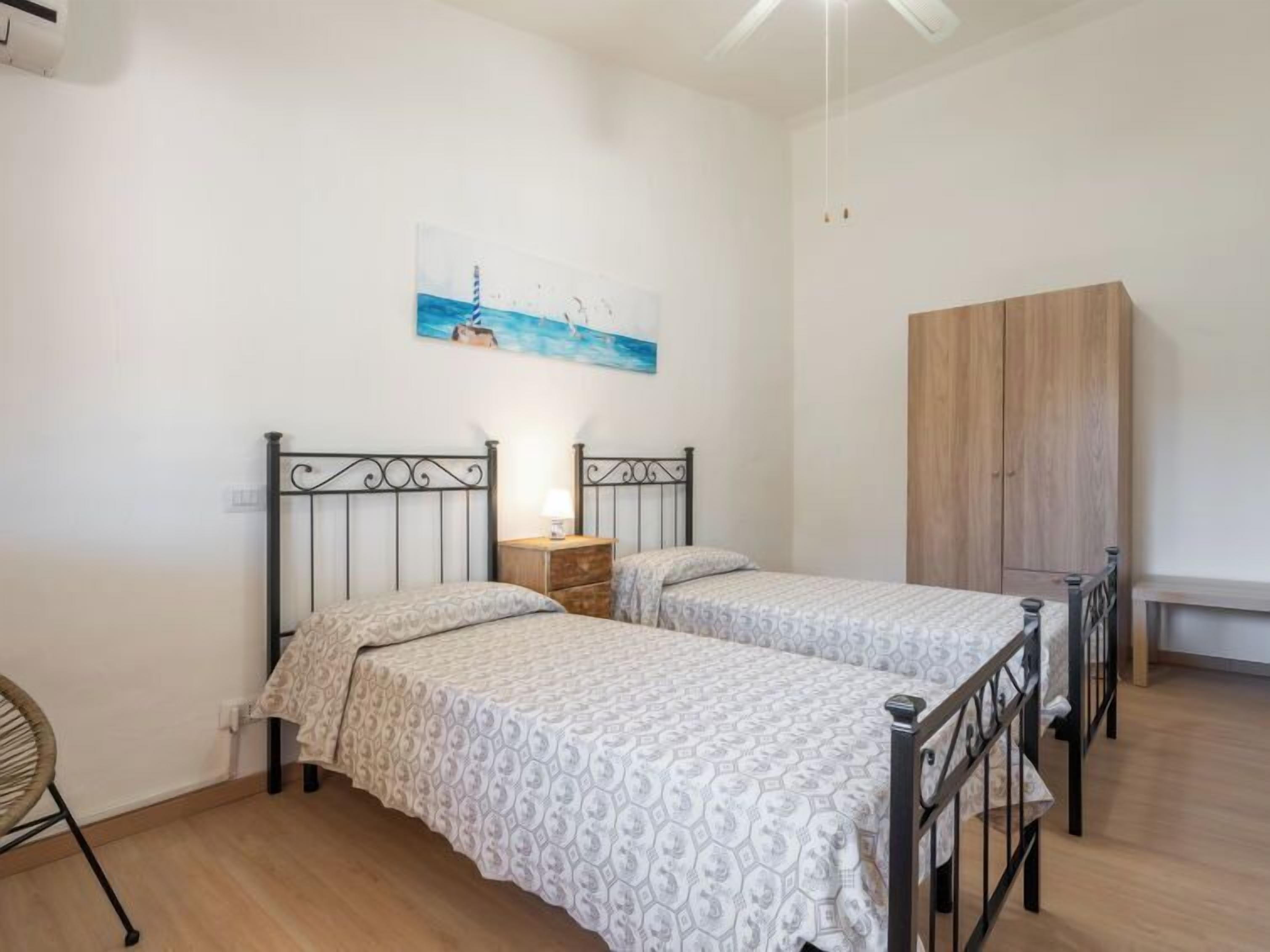 Un dormitorio con dos camas, un armario de madera, un cuadro en la pared y una silla.