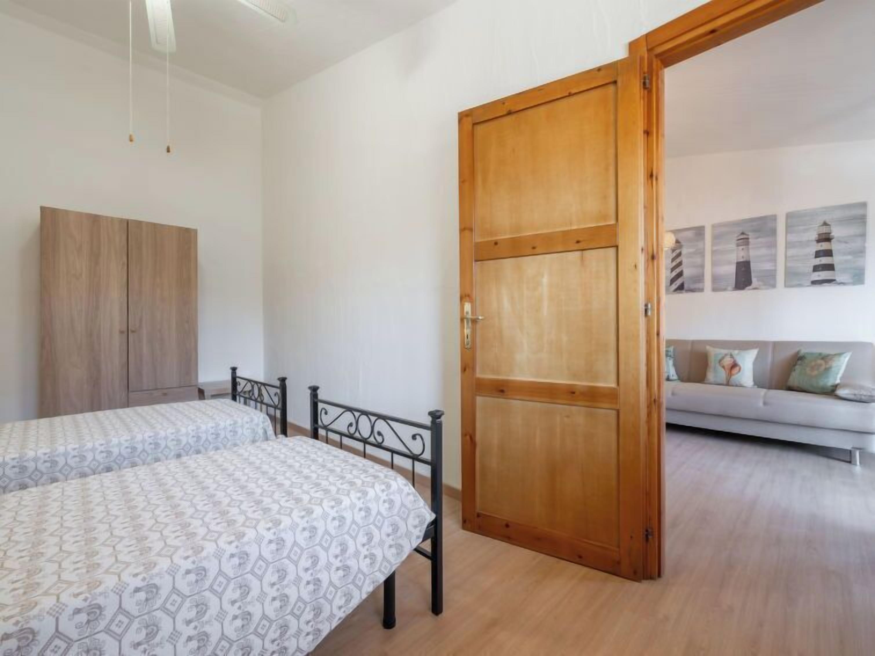 A bedroom with two beds, a wardrobe, and a door leading to another room.