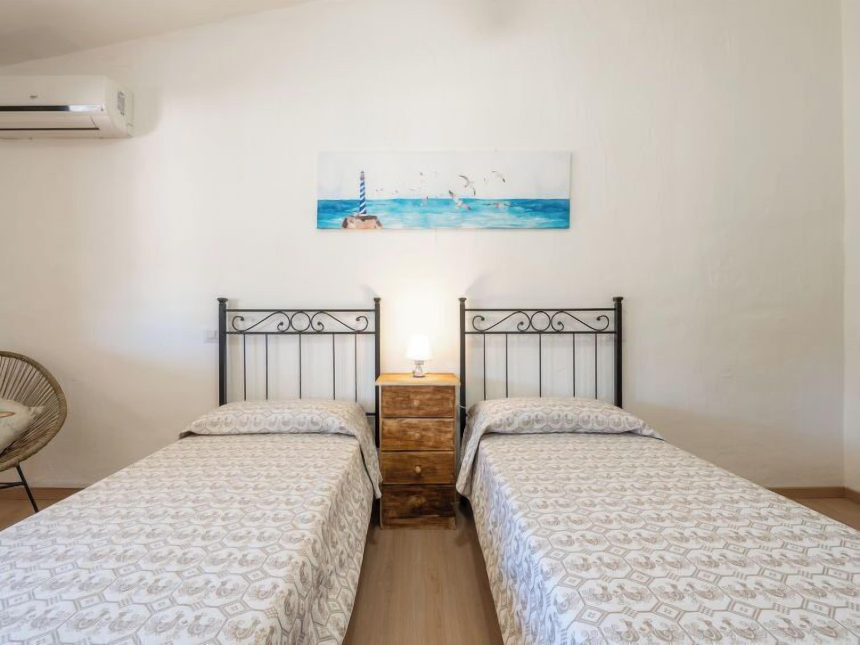 Une chambre avec deux lits, une table de chevet en bois, une chaise et un tableau représentant une scène de plage.