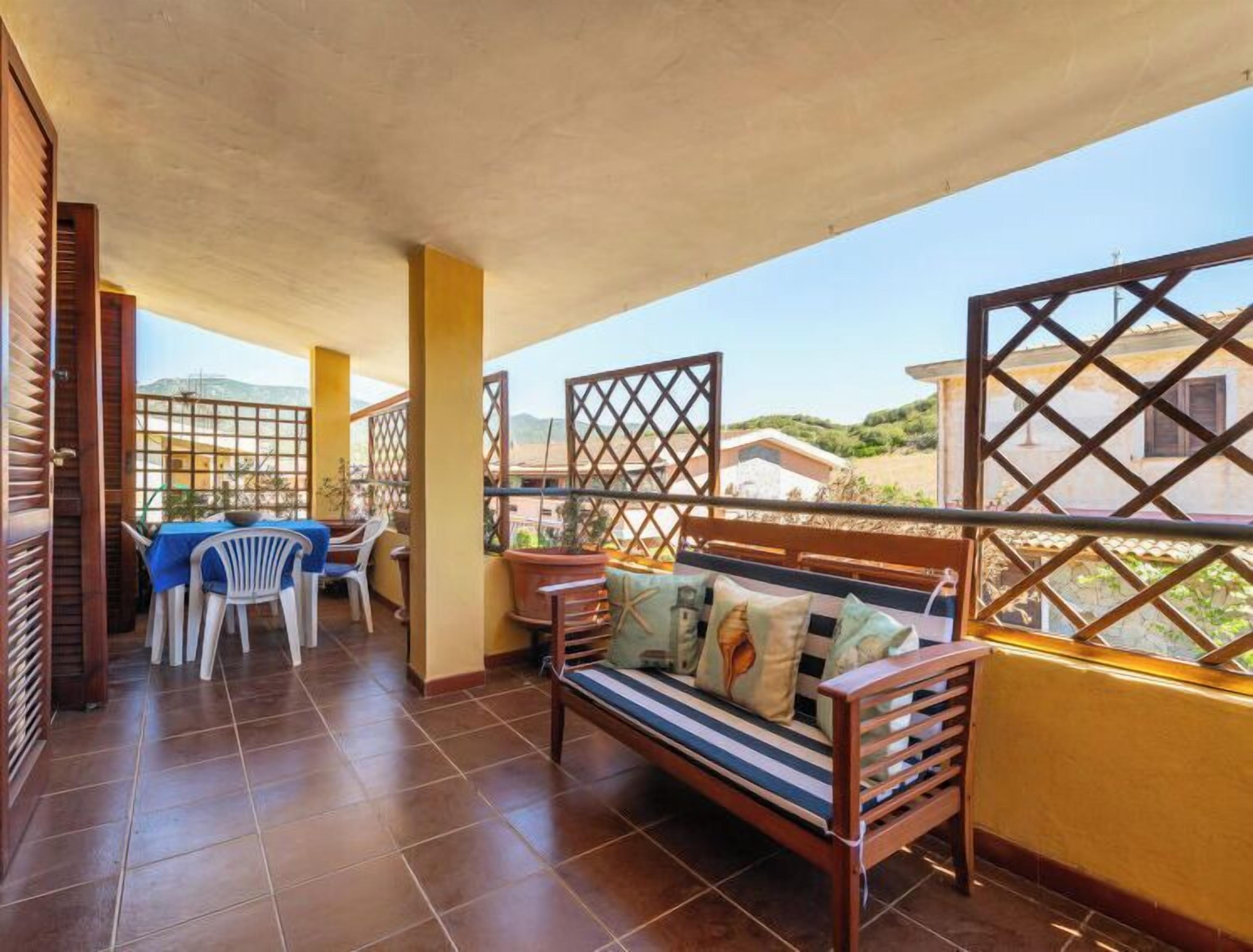 A balcony with a wooden bench, a table with chairs, and a view of the surrounding area.