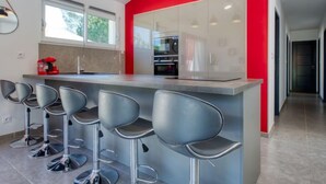 A modern kitchen with a red accent wall, stainless steel appliances, and bar stools.