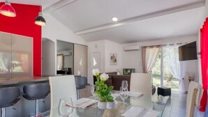 A modern dining area with a glass table, white chairs, and a red accent wall.