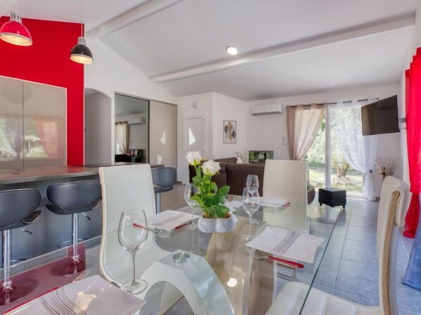 A modern dining area with a glass table, white chairs, and a red accent wall.
