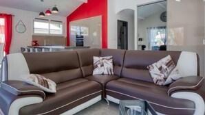 A modern living room with a brown and white sectional sofa, a glass coffee table, and a red accent wall.