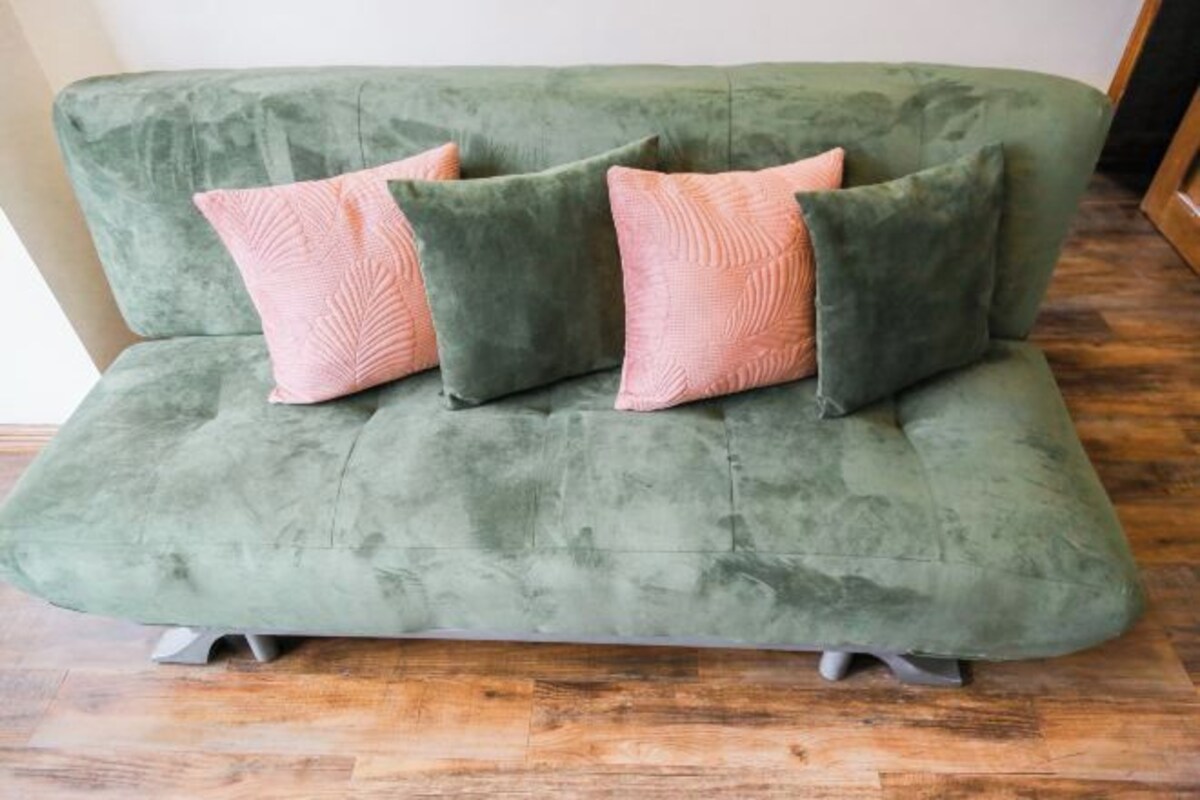 A green sofa with four pink pillows.