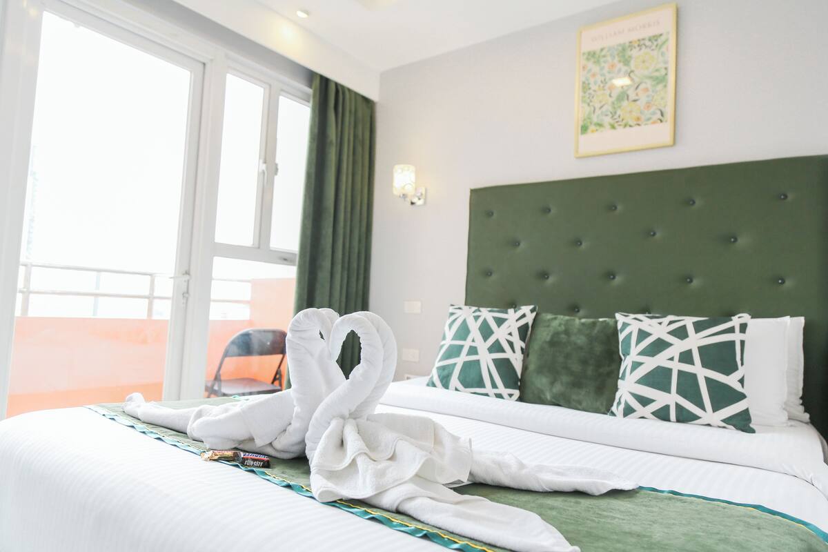 A hotel room with a bed, green curtains, a green headboard, and a framed picture on the wall.