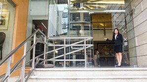 A woman standing on a glass balcony with metal railings, overlooking a cityscape. - Pacific Bay Grand Suites (Manila)