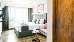 A hotel room with a bed, a bedside table with a lamp, a green sofa, and a wooden floor. - Pacific Bay Grand Suites (Manila)