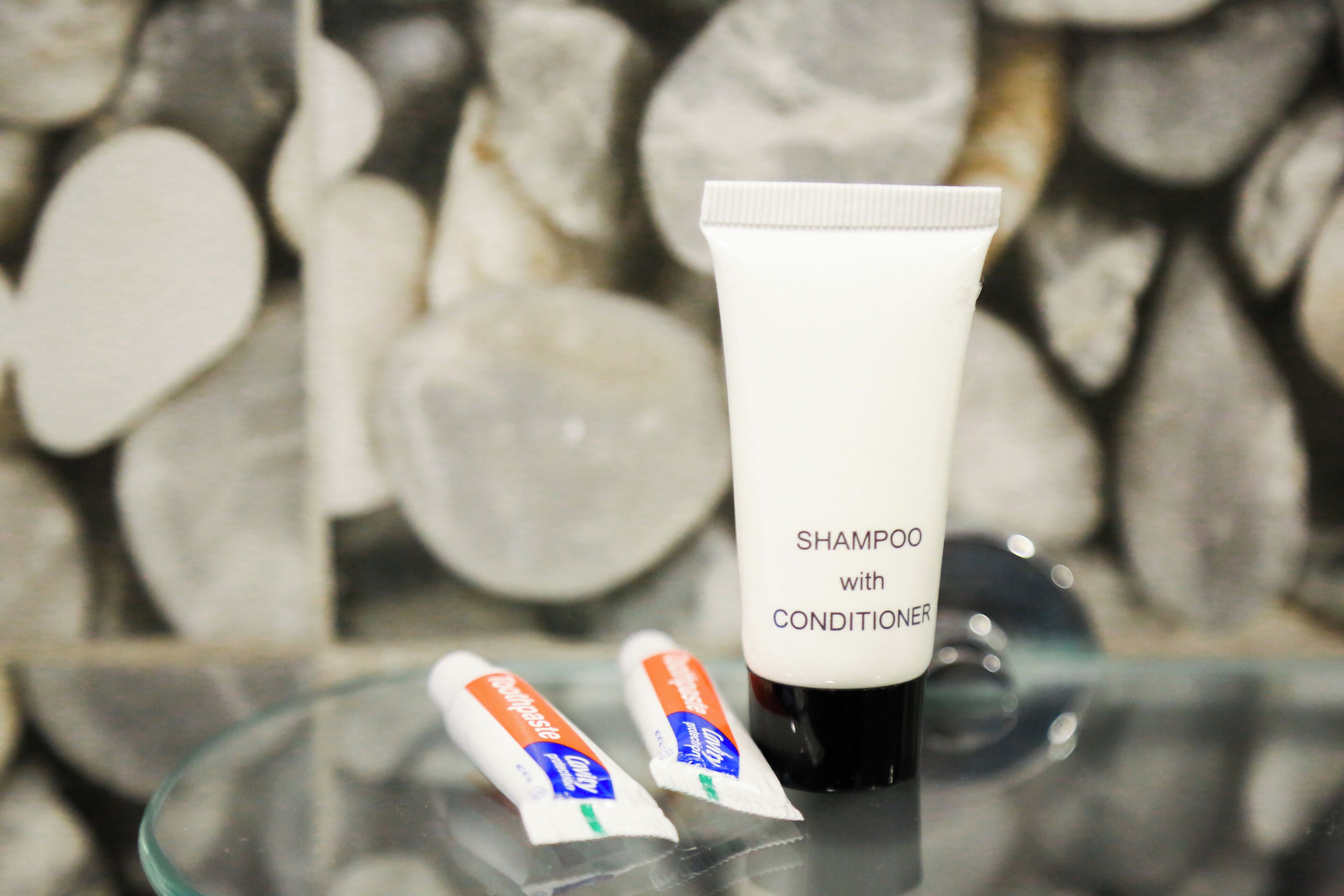 A tube of shampoo with conditioner on a glass surface with a blurred background of stones.