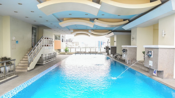 A swimming pool with a staircase leading to an upper level, a water filtration system, and a view of the surrounding buildings. - Pacific Bay Grand Suites (Manila)