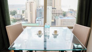 A glass-top table with two cups and two bottles of water, set between two chairs, with a view of tall buildings and a body of water through large windows. - Pacific Bay Grand Suites (Manila)