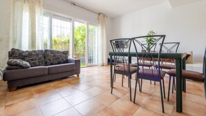 Un coin repas avec une table et des chaises, un canapé et une vue sur l’extérieur à travers une porte vitrée.