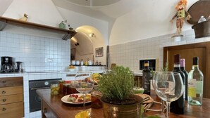 A kitchen with white tiles, a wooden countertop, a coffee maker, a wine bottle, and a potted plant. - Casa Sylvie by Interhome (Lucinasco)
