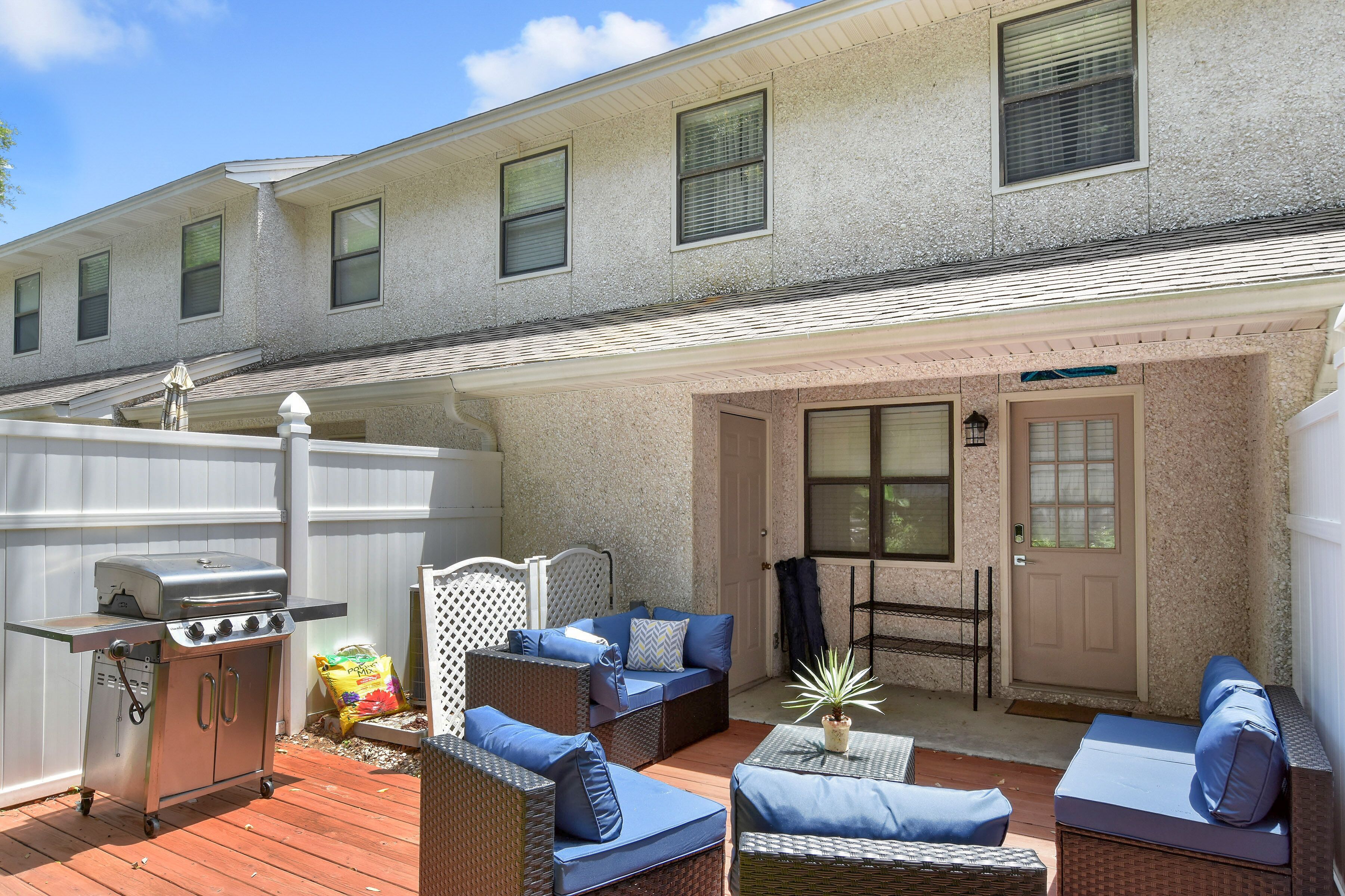 A covered patio with outdoor furniture, a grill, and a door leading to a building.
