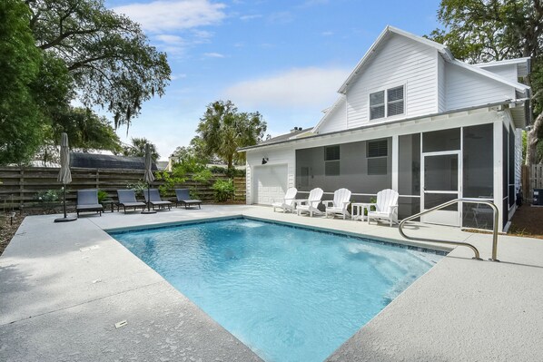 A swimming pool with a covered patio area, outdoor chairs, and a white house with large windows. - Large Heated Pool • Walk to Restaurants • 2 King Ensuites • EV Charger (St Simons)