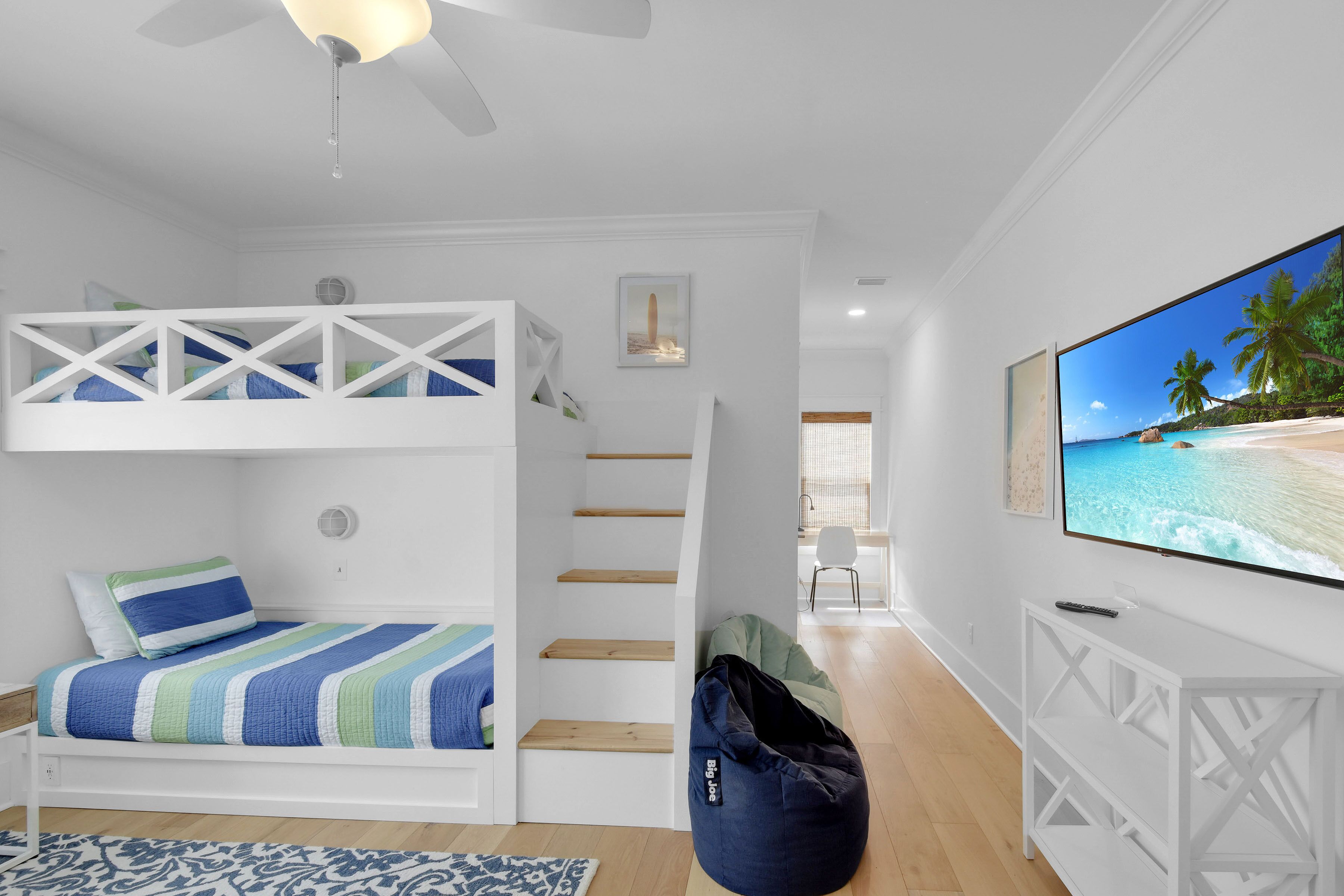A bedroom with a bunk bed, a flat-screen TV, a bean bag, and a staircase.