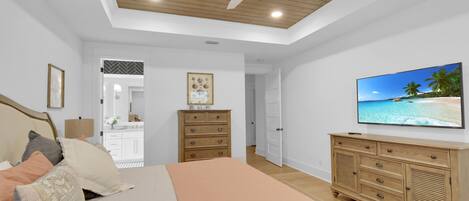 Un dormitorio con cama, cómoda de madera, televisor, ventilador de techo y vista al mar a través de la ventana.