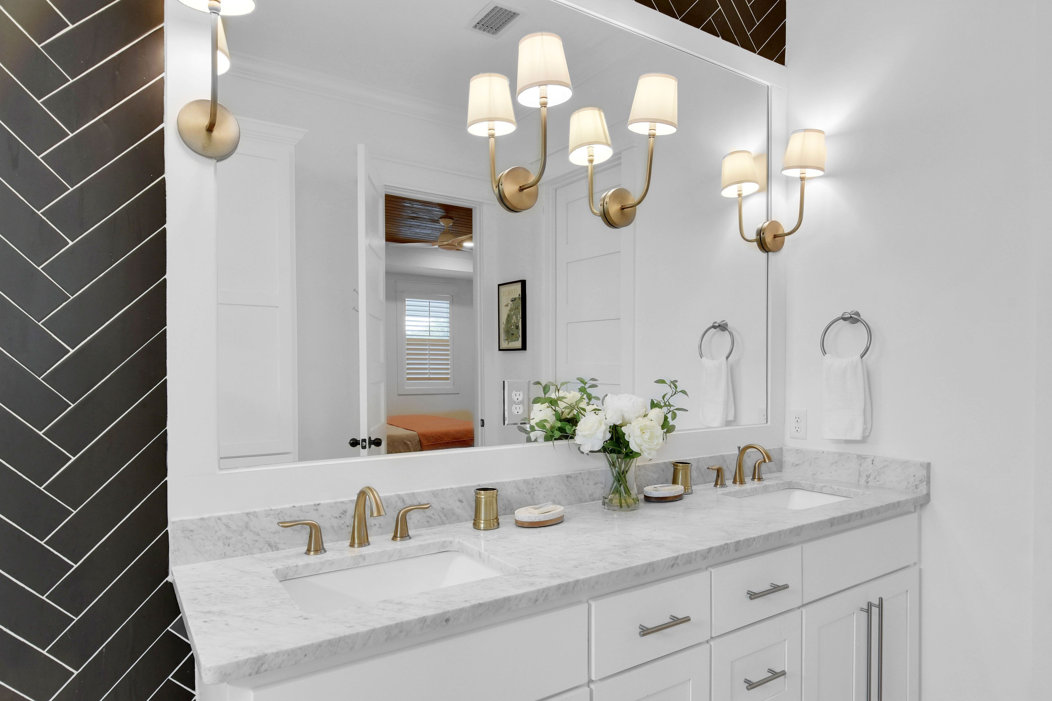 A modern bathroom with two sinks, gold fixtures, and a large mirror with wall-mounted lights.