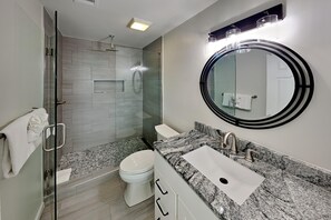 Een moderne badkamer met een douche met glazen wand, een ronde spiegel en een granieten aanrecht.