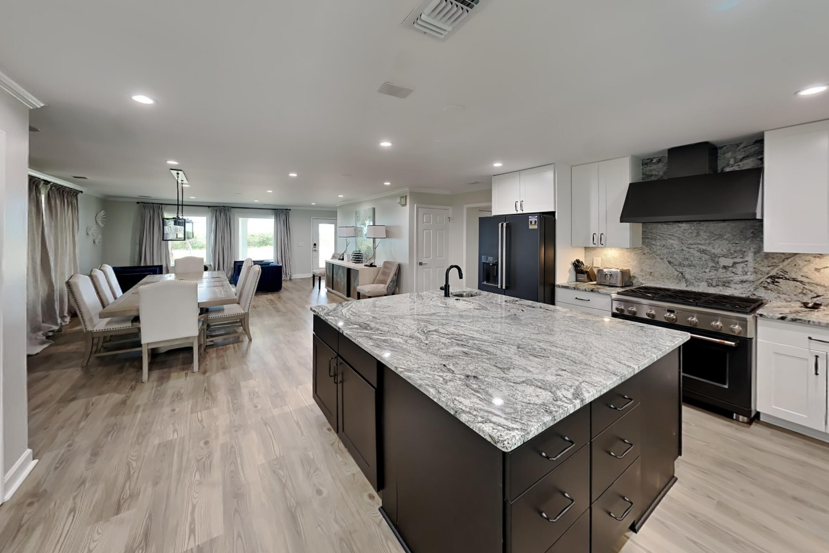 A modern kitchen with a marble island, dark cabinets, and a stainless steel range hood.