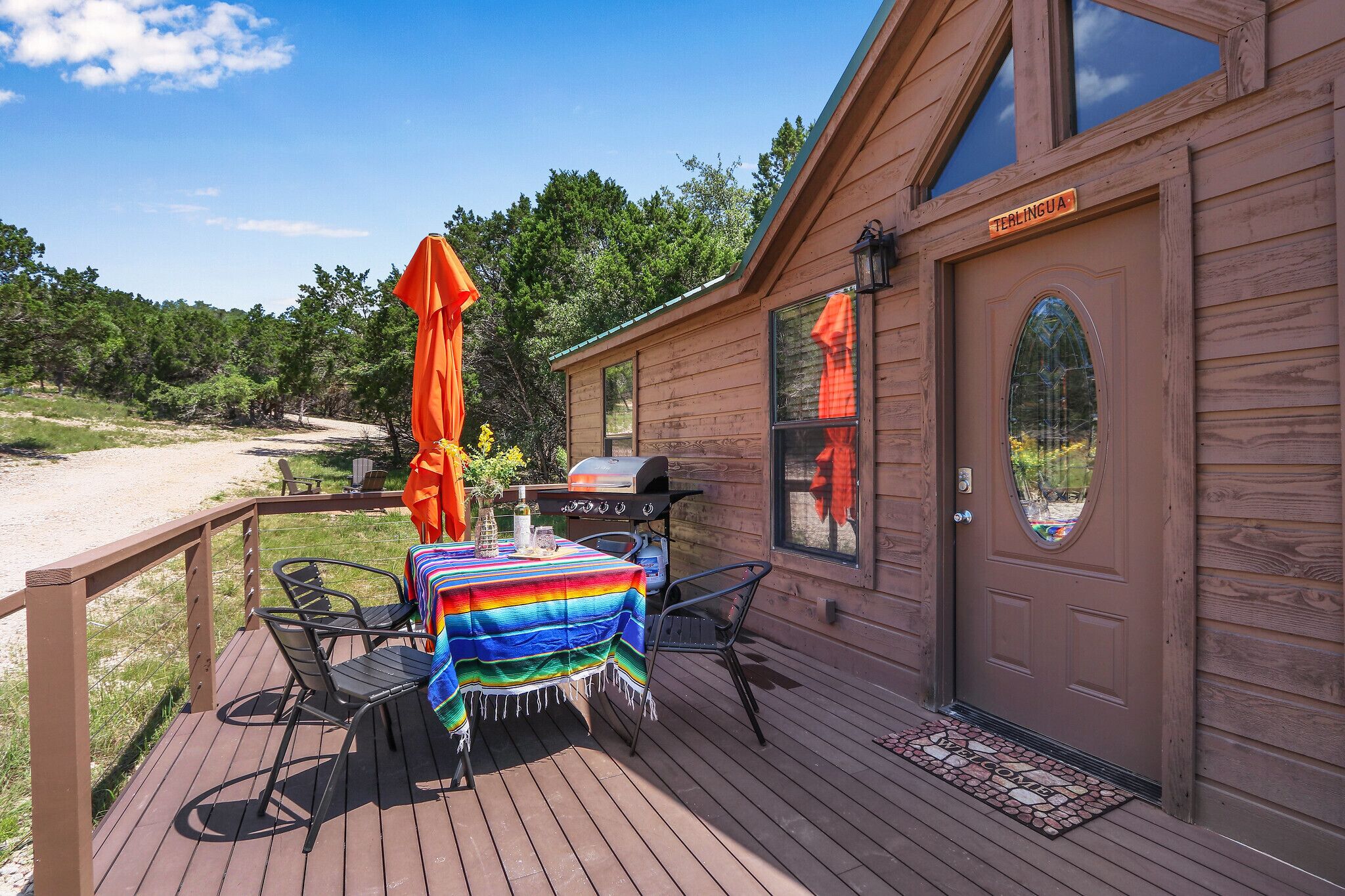 A wooden cabin with a deck, a barbecue grill, and a table with a colorful tablecloth.