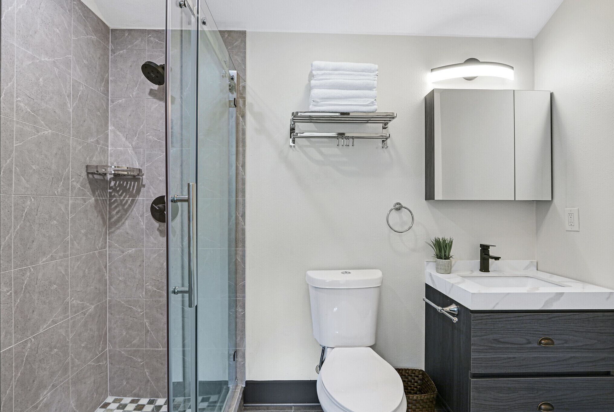 Une salle de bain moderne avec une douche à parois de verre, des toilettes blanches, un meuble-lavabo avec un miroir et un porte-serviettes.