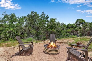 Un terrain de camping équipé de deux fauteuils Adirondack, d’un foyer et d’un banc en bois.
