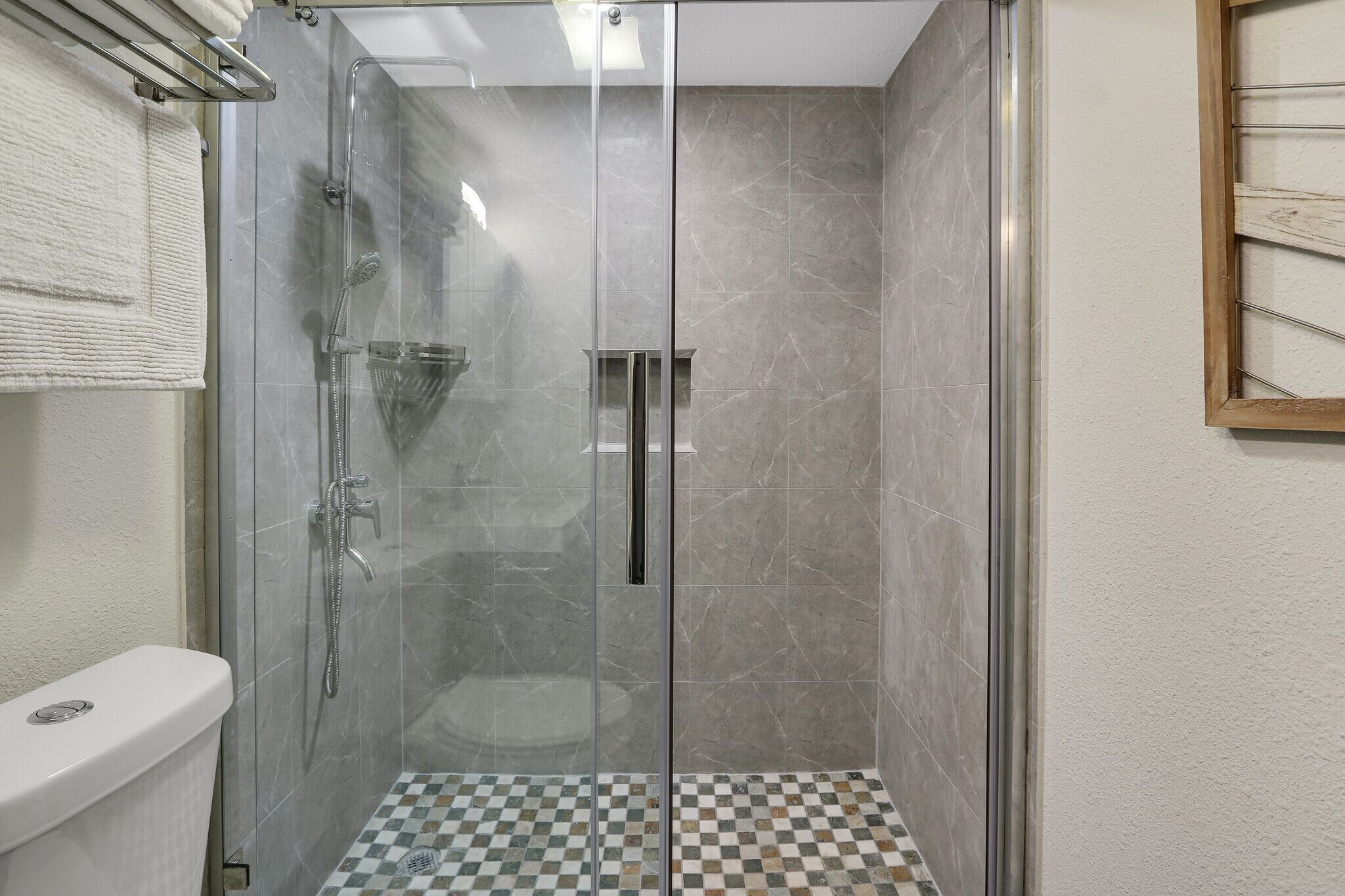 Eine Duschkabine mit Glas, gefliestem Boden und einer Toilette links.