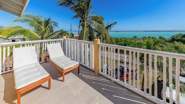 A balcony with two lounge chairs, a white railing, and a view of the ocean and palm trees. - Lagoon Views, Private Balcony & Near the Beach (Bottle Creek)