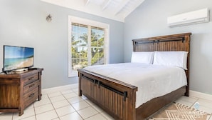 A bedroom with a wooden bed, a TV on a wooden dresser, a window with blinds, and an air conditioner on the wall. - Lagoon Views, Private Balcony & Near the Beach (Bottle Creek)