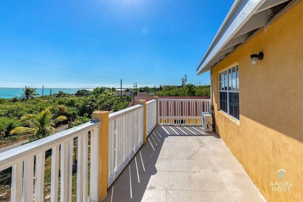 A balcony with a view of the ocean, a yellow building, and a white railing.