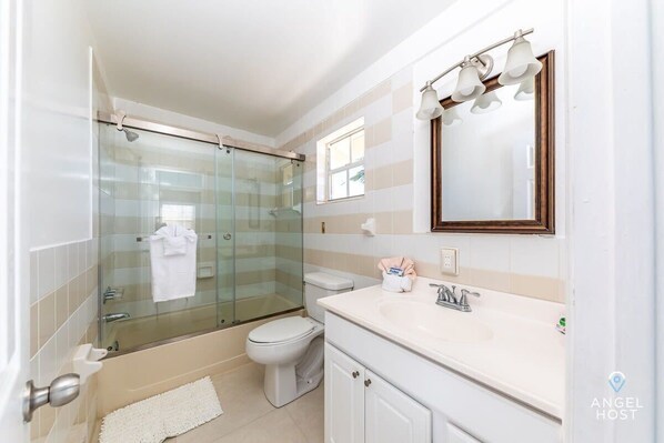 A modern bathroom with a glass-enclosed shower, a toilet, a sink with a mirror, and a small window.