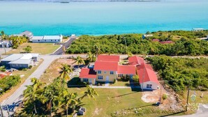 An aerial view of a coastal property with a prominent red-roofed house, surrounded by lush greenery and a clear view of the turquoise sea. - Lagoon Views, Private Balcony & Near the Beach (Bottle Creek)
