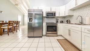A modern kitchen with white cabinets, stainless steel appliances, and a tiled floor. - Lagoon Views, Private Balcony & Near the Beach (Bottle Creek)