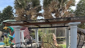A garden with a pergola, white columns, a metal fence, and a small pond. - Chez Lilie Maison d'hôtes à Saly (Mbour)