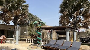 A poolside area with lounge chairs, a decorative snake sculpture, palm trees, and a pergola. - Chez Lilie Maison d'hôtes à Saly (Mbour)
