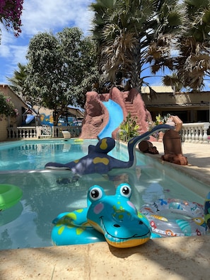 Una piscina con uno scivolo, un galleggiante a forma di rana e un murale.