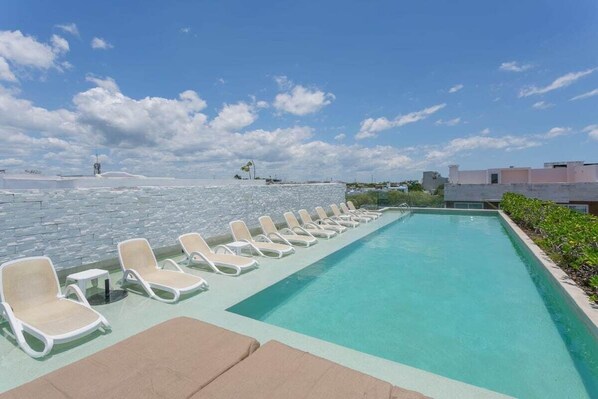 A rooftop pool with lounge chairs and a clear view of the city skyline.