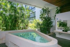 A modern outdoor pool area with lush tropical plants, a built-in hot tub, and a contemporary design.