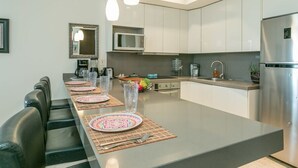 Een moderne keuken met witte kasten, een roestvrijstalen koelkast en een eethoek met een lange tafel gedekt voor vier personen.