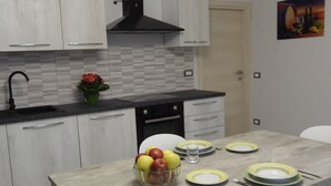 A modern kitchen with white cabinets, a black range hood, a tiled backsplash, and a dining table set with plates and cutlery. - 4 Bedroom Private vacation home in Govone (Govone)