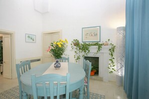 A dining room with a round table, blue chairs, a vase with flowers, a fireplace with climbing plants, and framed pictures on the walls. - Pat016 in Pat With 8 Bedrooms and 8 Bathrooms (Patu)
