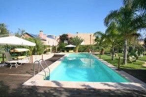 A rectangular swimming pool with a wooden deck, surrounded by palm trees and lounge chairs.