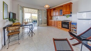 A modern kitchen with wooden cabinets, a gas stove, and a refrigerator. There is a dining area with a table and chairs, and a large window providing natural light. - And001 in Andrano With 4 Bedrooms and 2 Bathrooms (Andrano)