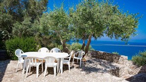 A stone patio with white plastic chairs and a table, overlooking a clear blue sea. - And001 in Andrano With 4 Bedrooms and 2 Bathrooms (Andrano)