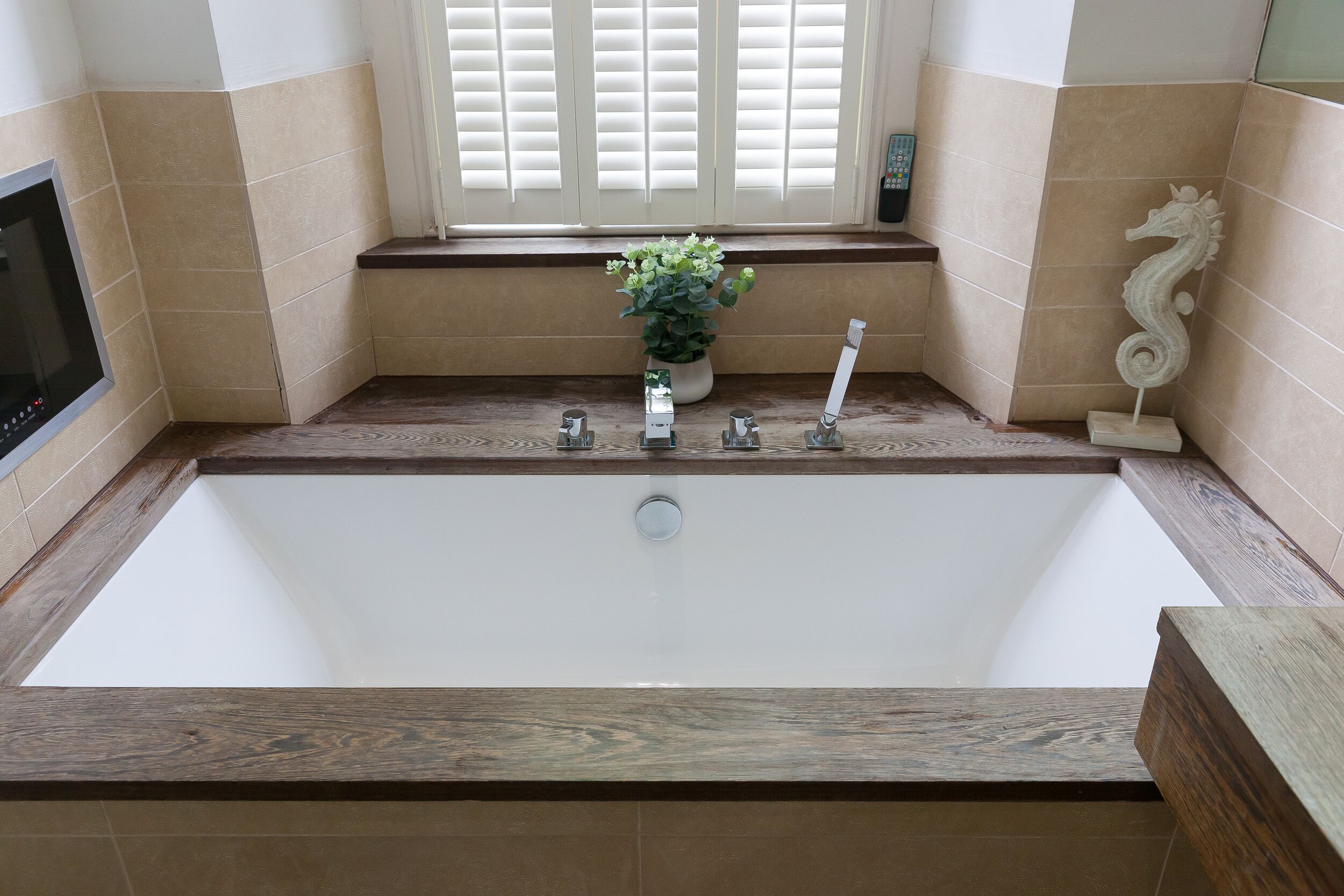 A bathroom with a large bathtub, a potted plant, a decorative seahorse, and a remote control on the windowsill.