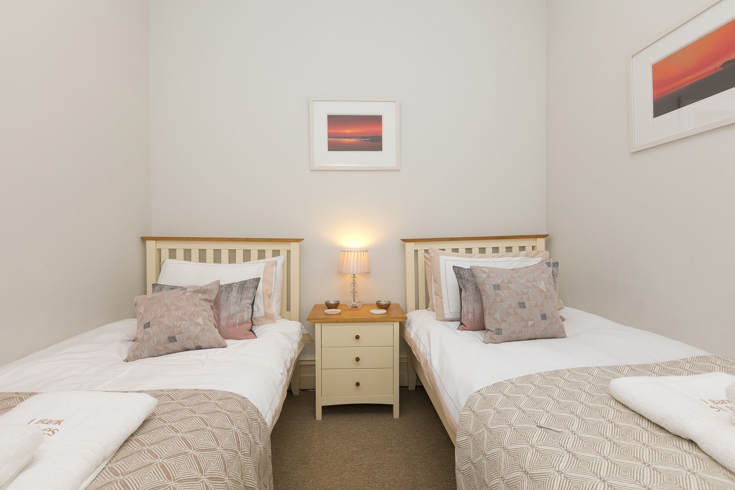 A twin room with two beds, a bedside table with a lamp, and a framed picture on the wall.